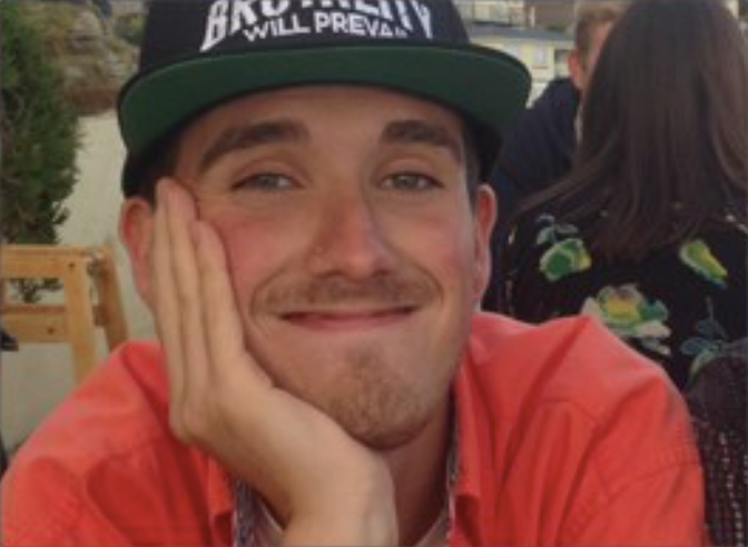male smiling eith his head in his hands, wearing a snapback