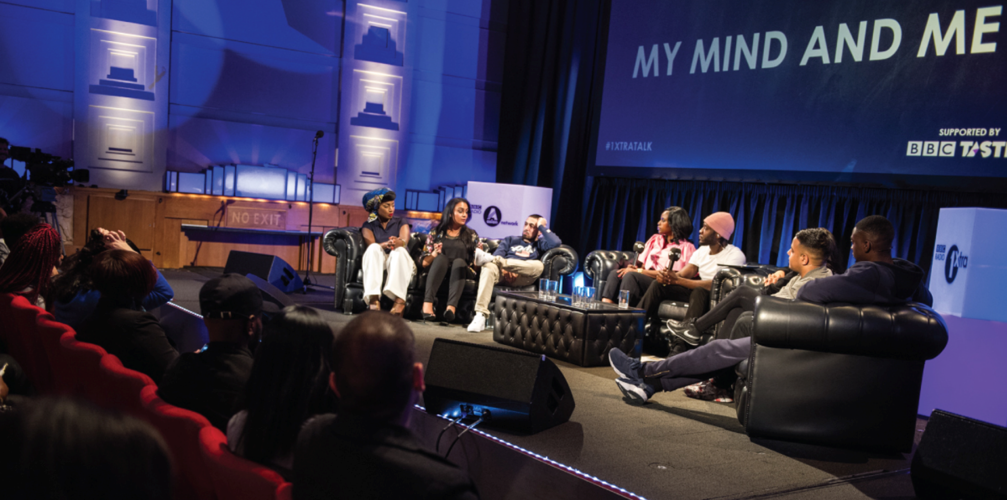 A group of people sitting on sofas on a stage, speaking to the audience and each other