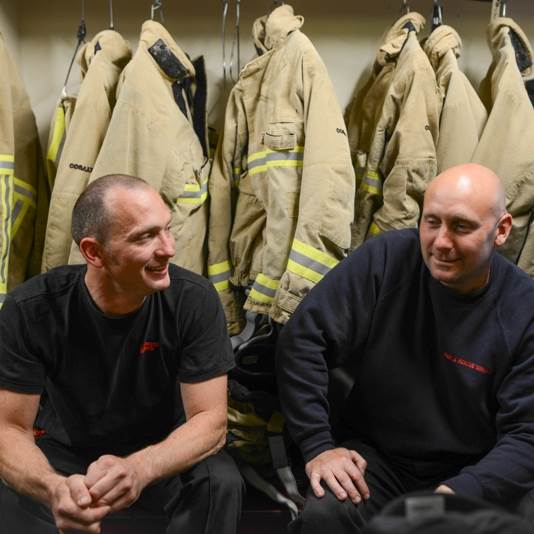 Two firefighters sat in front of firefighter coats