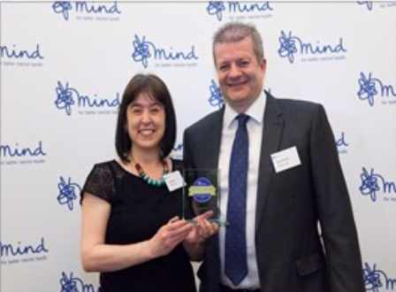 Man and woman, with her holding the award, standing together in front of a wall of Mind logos