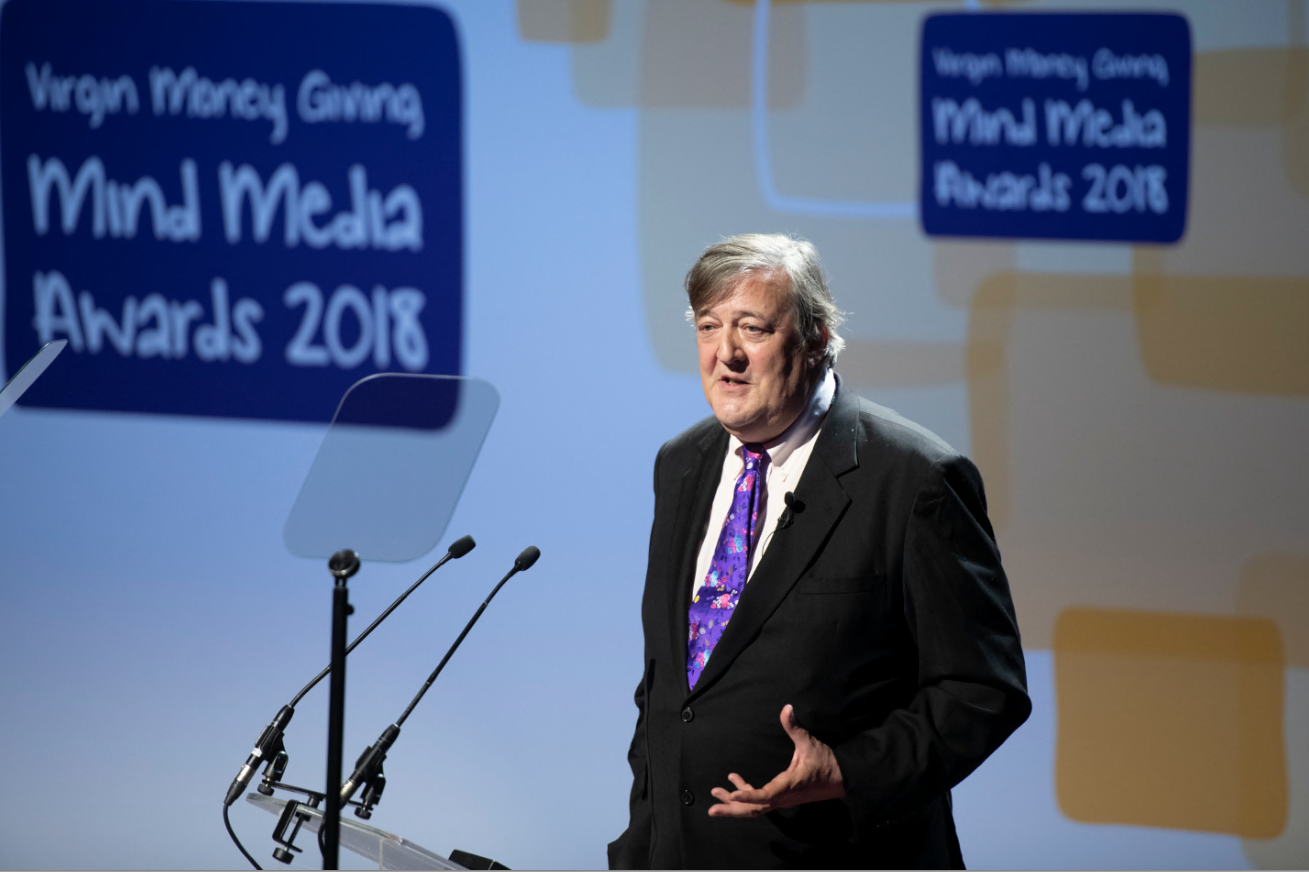 Steven Fry at the Media Mind Awards talking into microphones on a podium