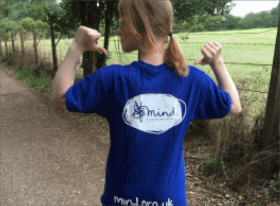 Female pointing at her Mind branded top whilst walking past fields