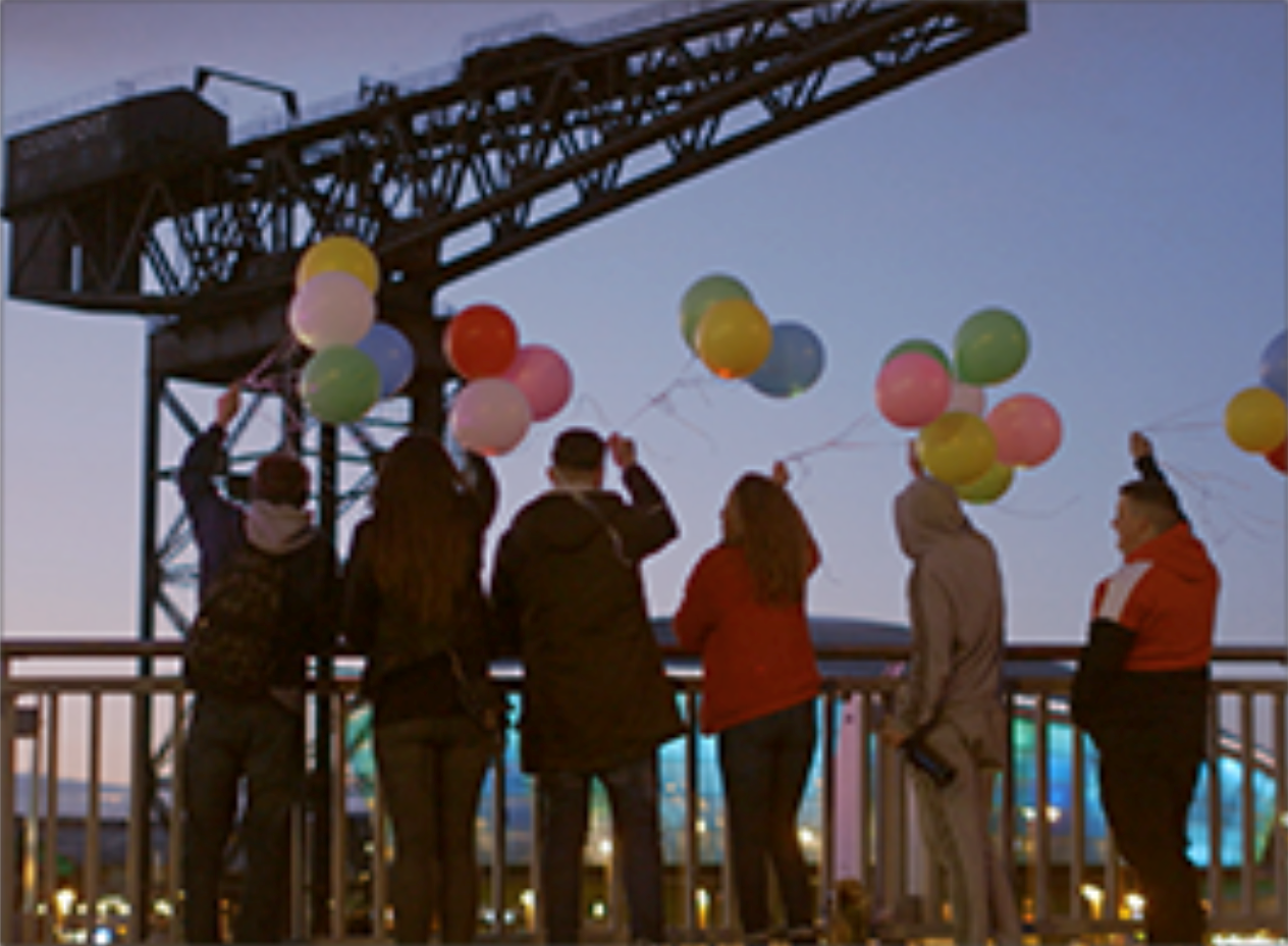 Group of people looking out to sea holding colourful balloons in the air