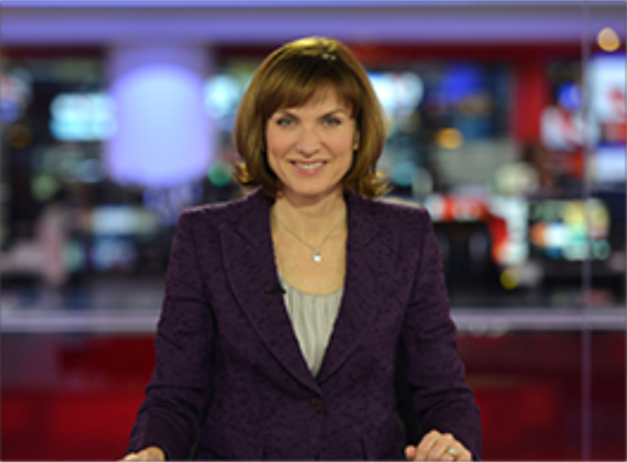 A female news presenter on set, smiling at the camera