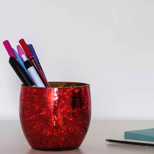 Red shiny pen pot with pens in on table with notebooks