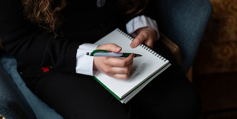 Close Up Of Person Writing In Note Pad