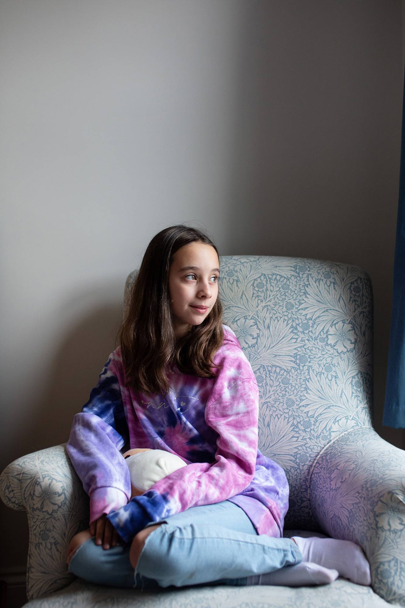 Close Up Of Young Girl Sat In Chair Looking To The Right Looking Pensive