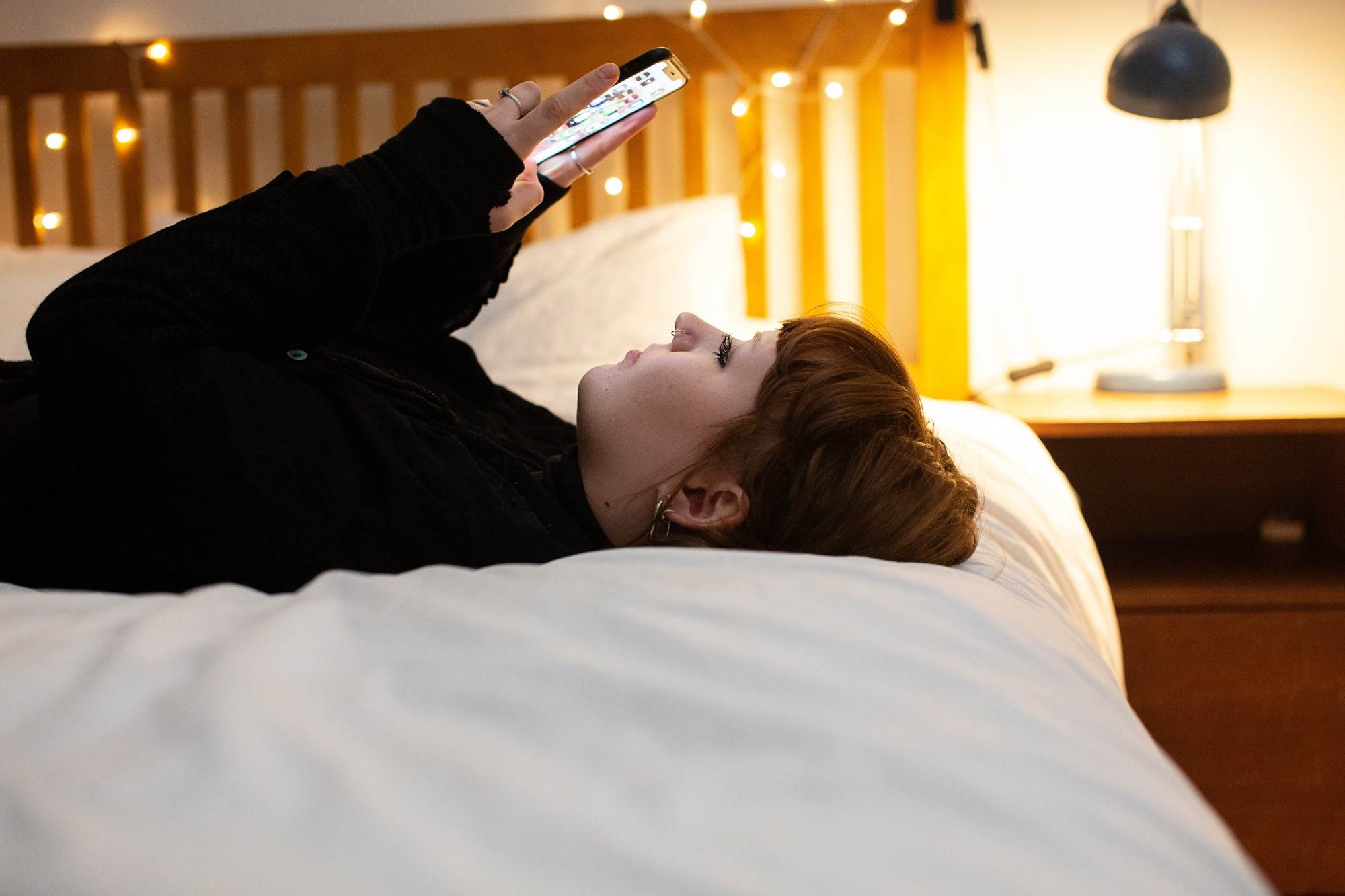 Girl Lying On Side On Bed Looking At Phone
