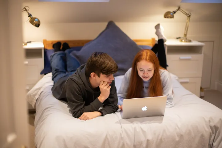 Teen Boy And Girl Discussing Laptop Content Lying On Bed