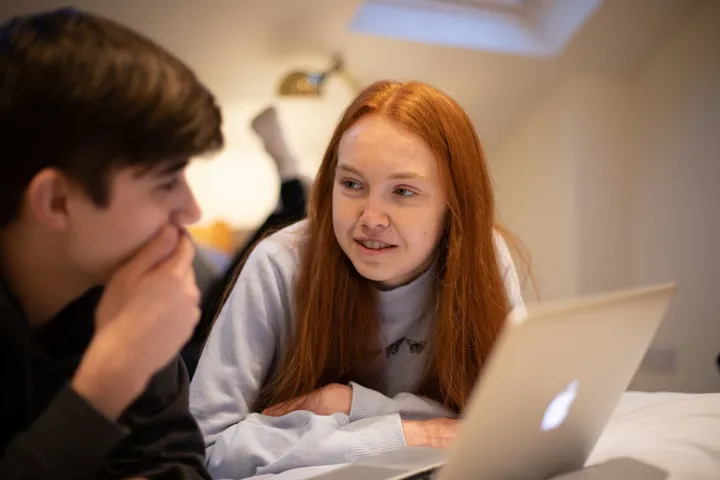 Teen Boy Talking To Teen Girl In Front Of Laptop Lying On Bed
