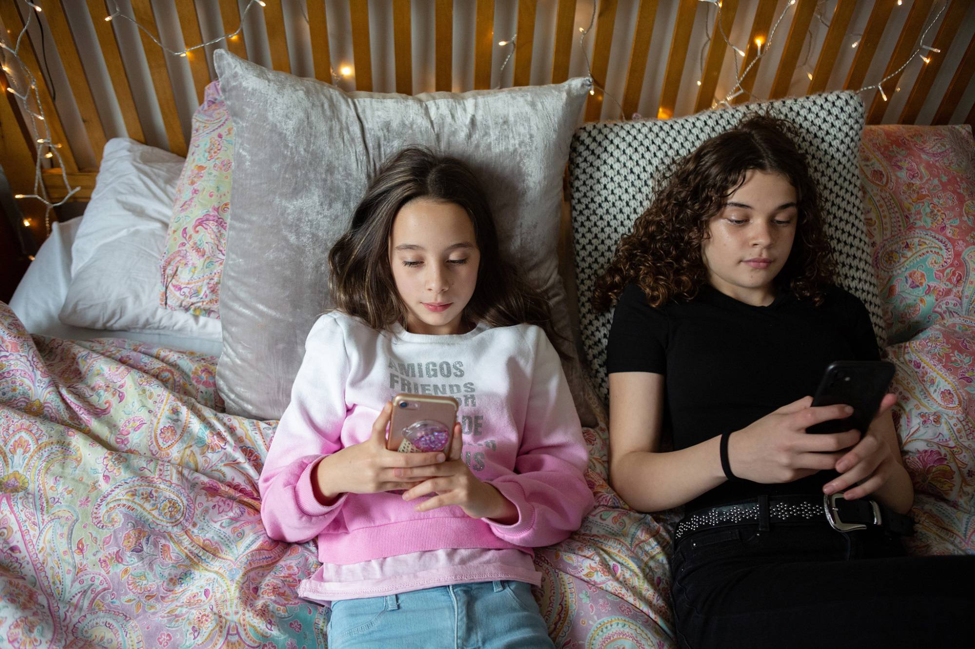 Teen Girl And Young Girl Use Phones While Lying On Bed