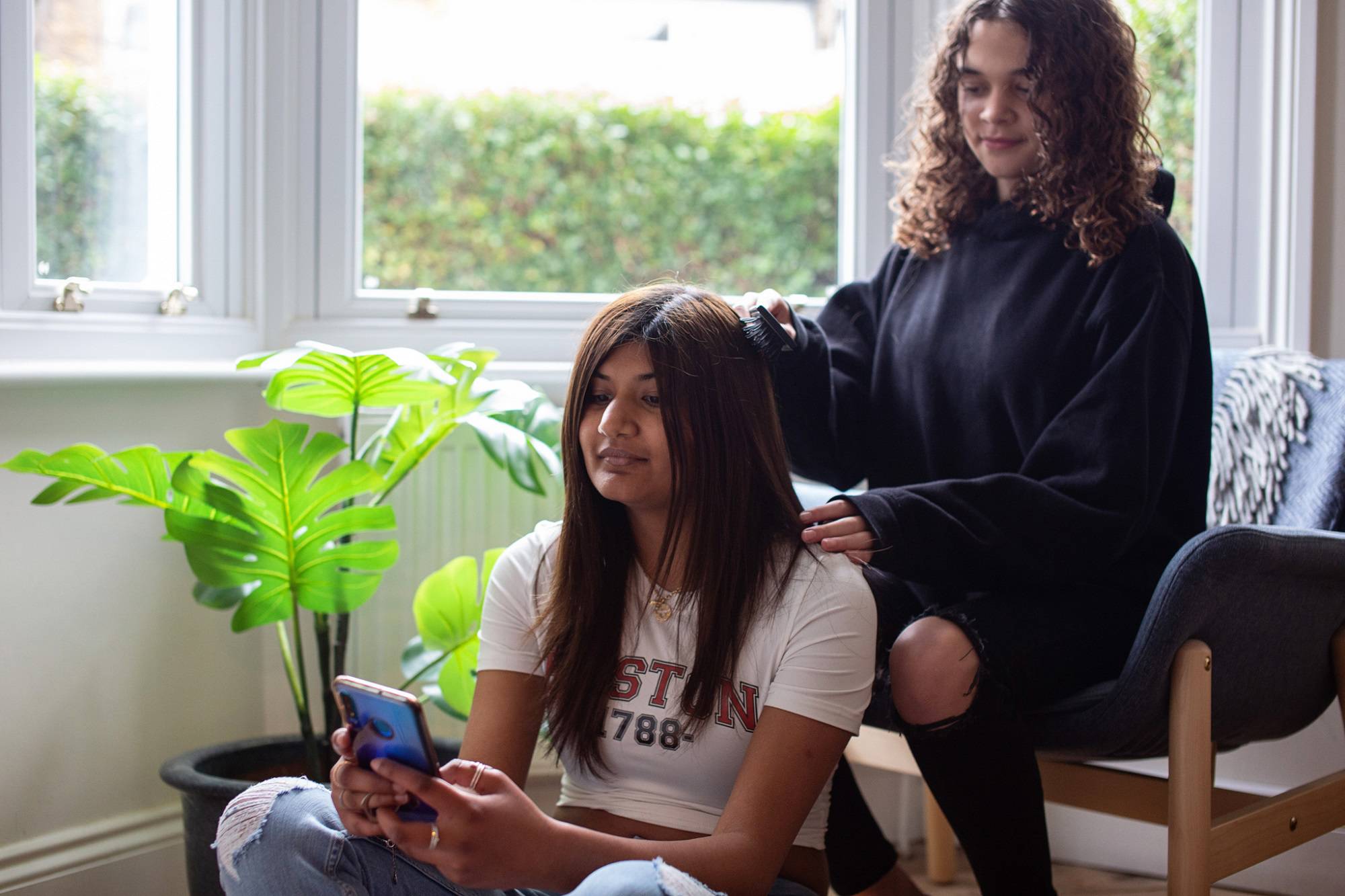 Teen Girl Brushes Other Teen Girls Hair Sat In Window