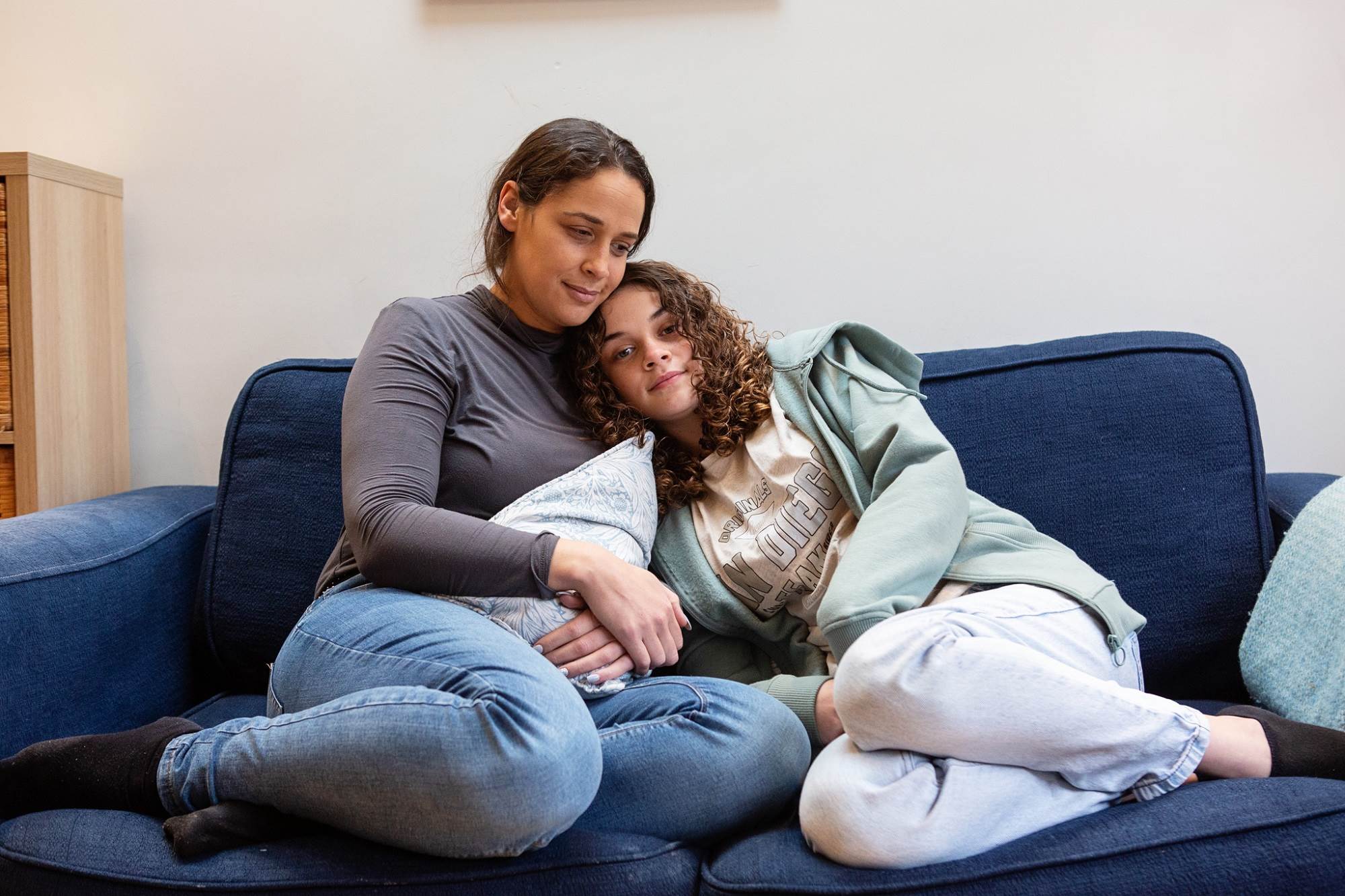 Teen Girl Cuddles Up To Woman On Sofa Smiling