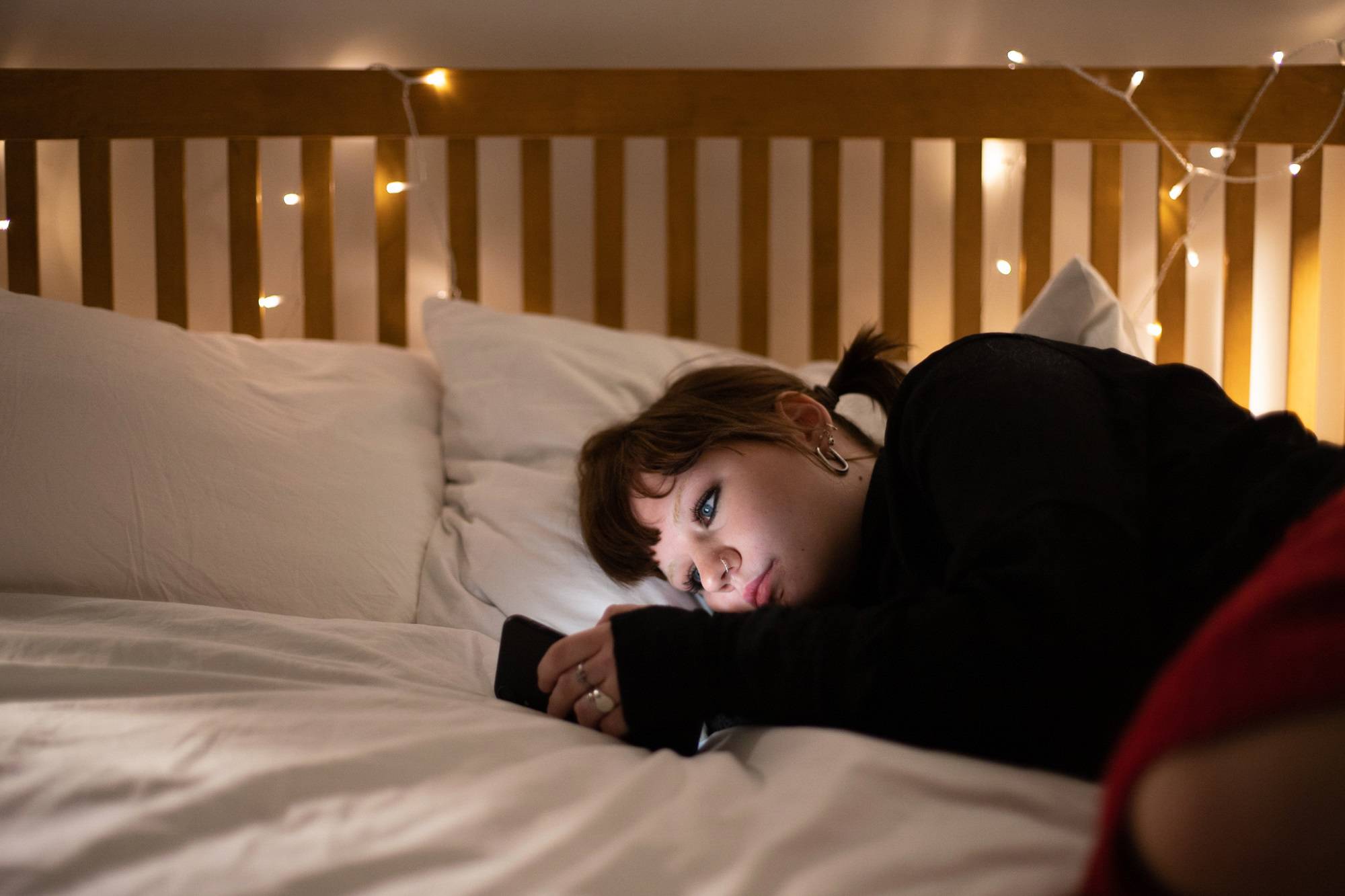 Teen Girl Reading Content On Phone Lying On Side On Bed Pensive