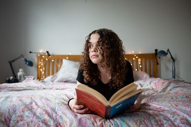 Teen Girl Reading On Bed Looks Away To The Left