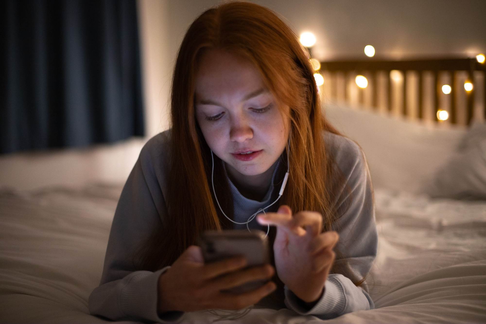 Teen Girl Scrolling On Phone Lying On Her Bed