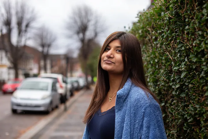 Teen Girl Stands In Street By Hedge Looking At Camera