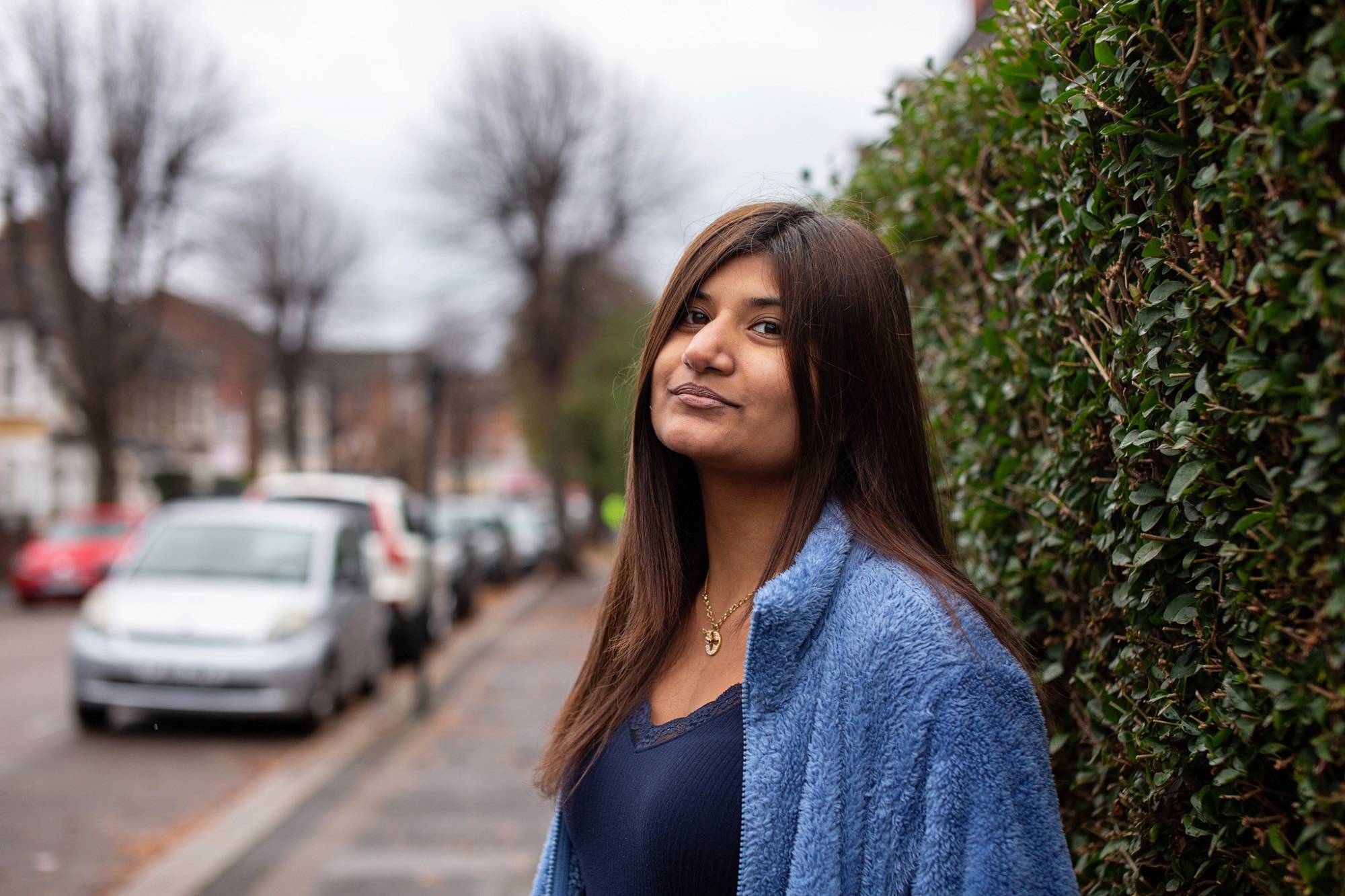 Teen Girl Stands In Street By Hedge Looking At Camera