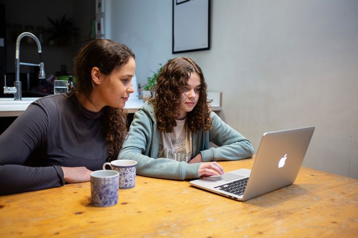 Teen Girl Uses Laptop With Woman At Table