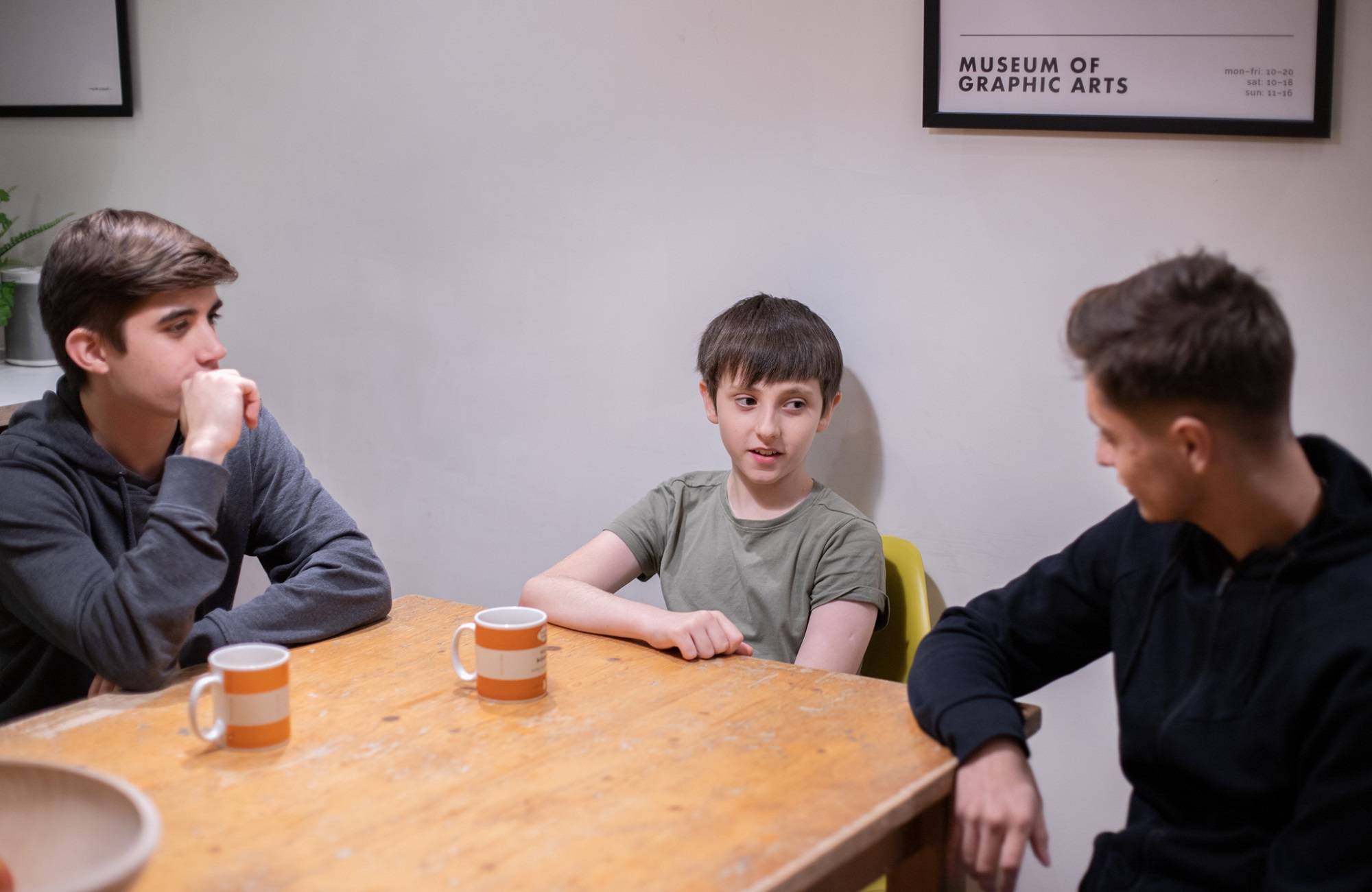 Two Teenage Boys And One Younger Boy Talking Around Table With Tea