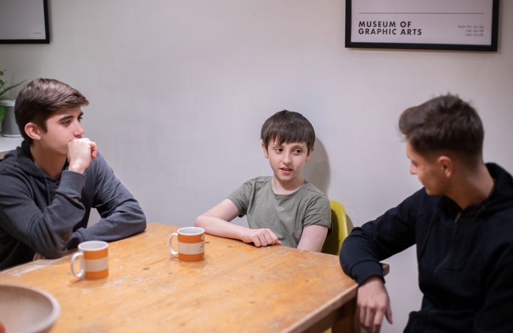 Two Teenage Boys And One Younger Boy Talking Around Table With Tea
