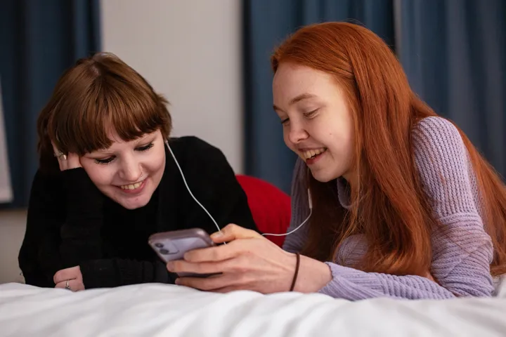 Two Teenage Girls Lying On Bed Listening To Music On Phone Smiling