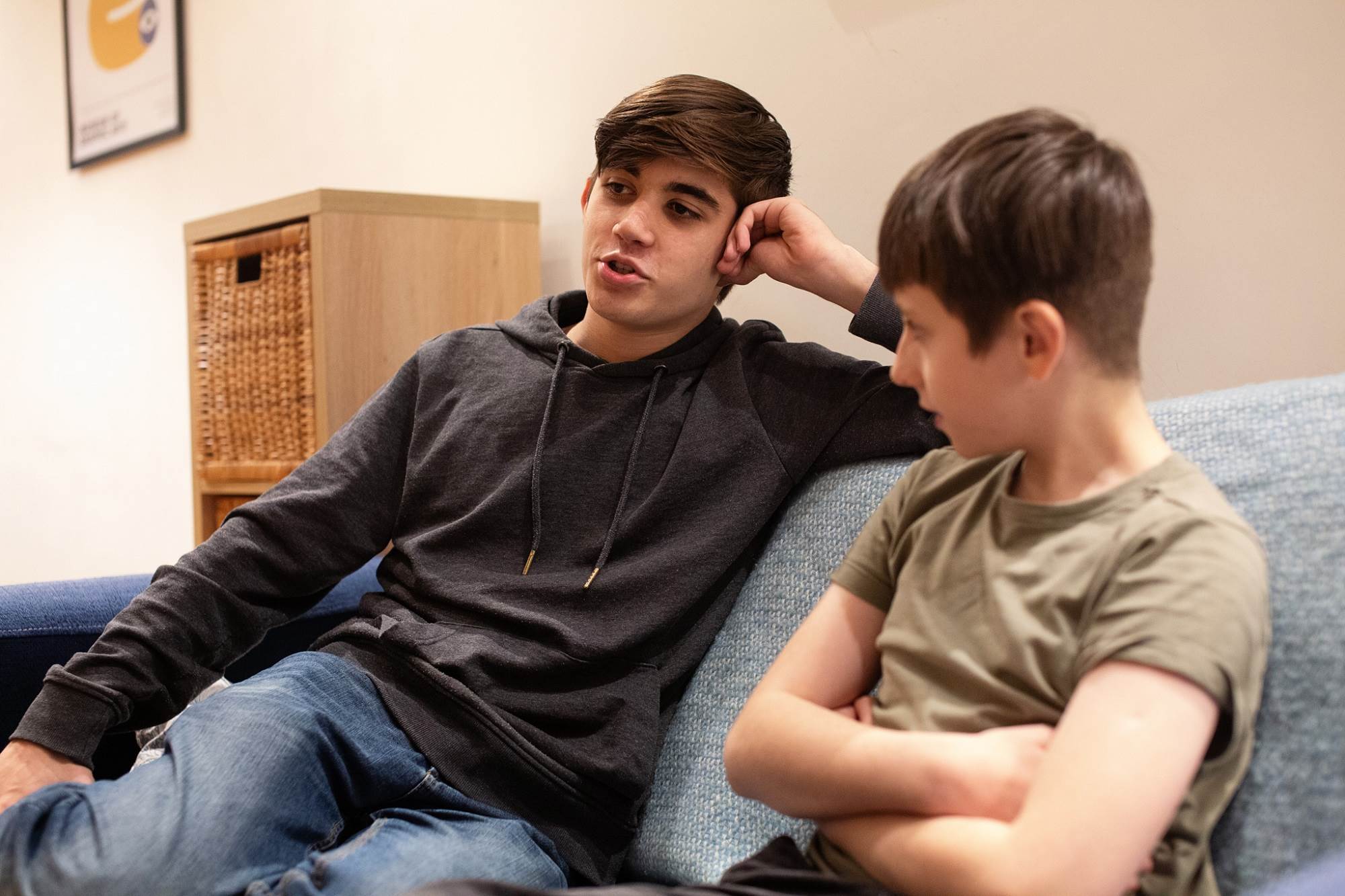 Young Boy And Teenage Boy Talking Sat On Sofa