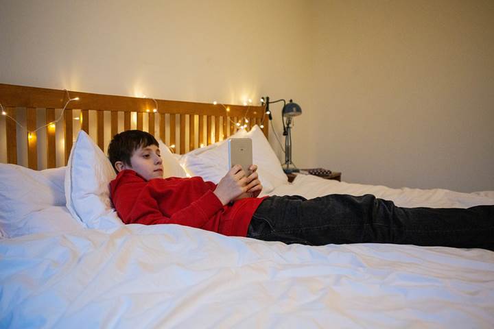 Young Boy Reading Mobile Content Lying On Bed