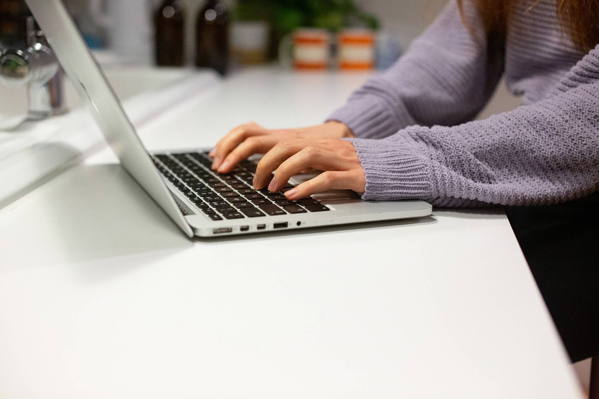 Young Person In Lavender Jumper Typing On Laptop
