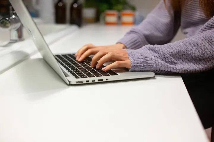 Young Person In Lavender Jumper Typing On Laptop Young Person In Lavender Jumper Typing On Laptop