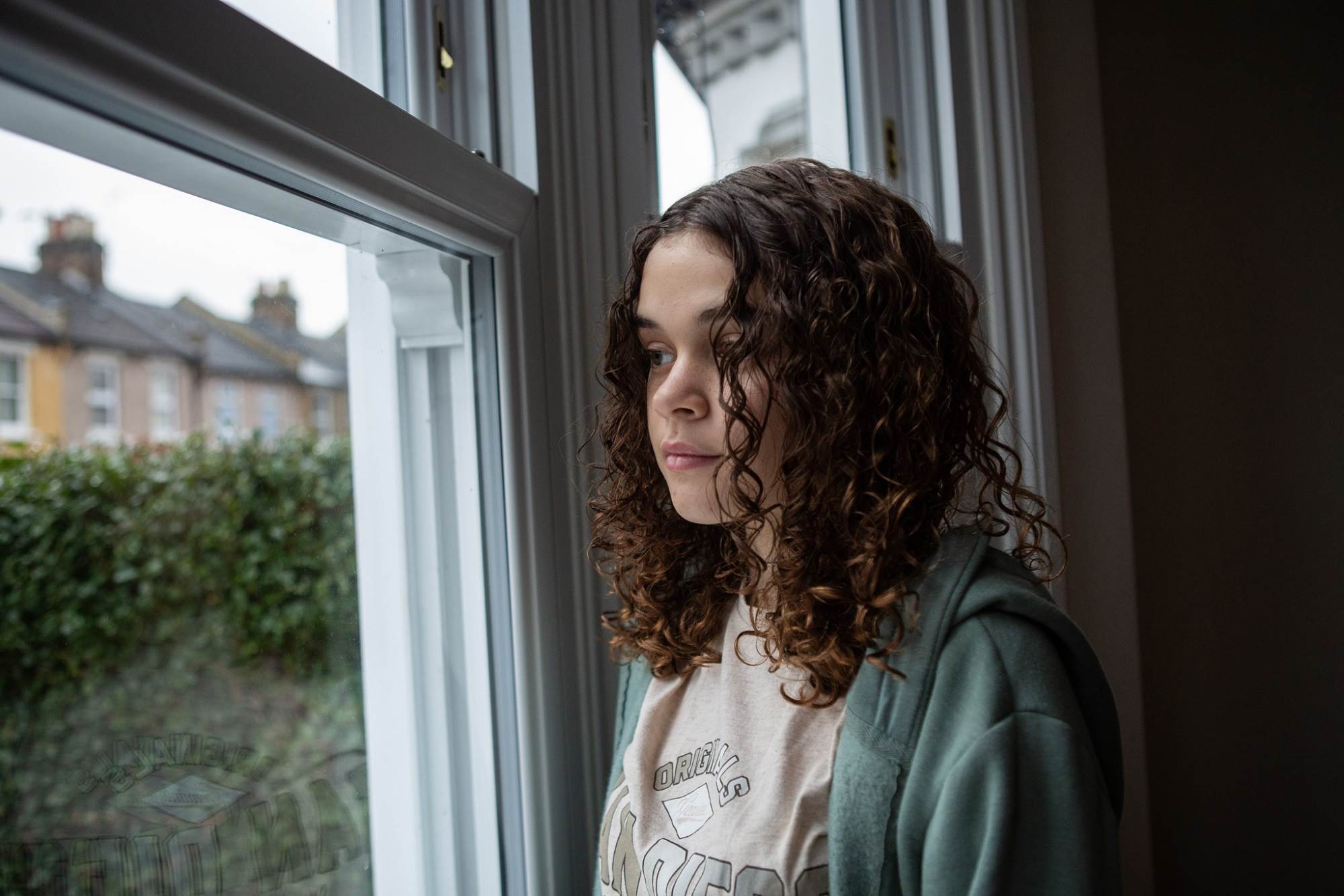 Young Teen With Curly Hair Looks Through Window