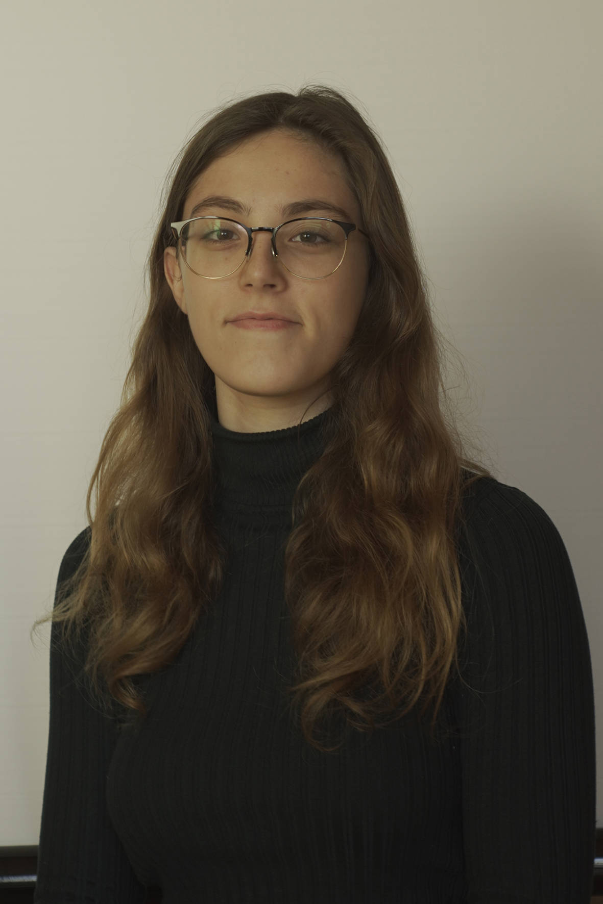 White woman with long brown hair wearing glasses looks at the camera
