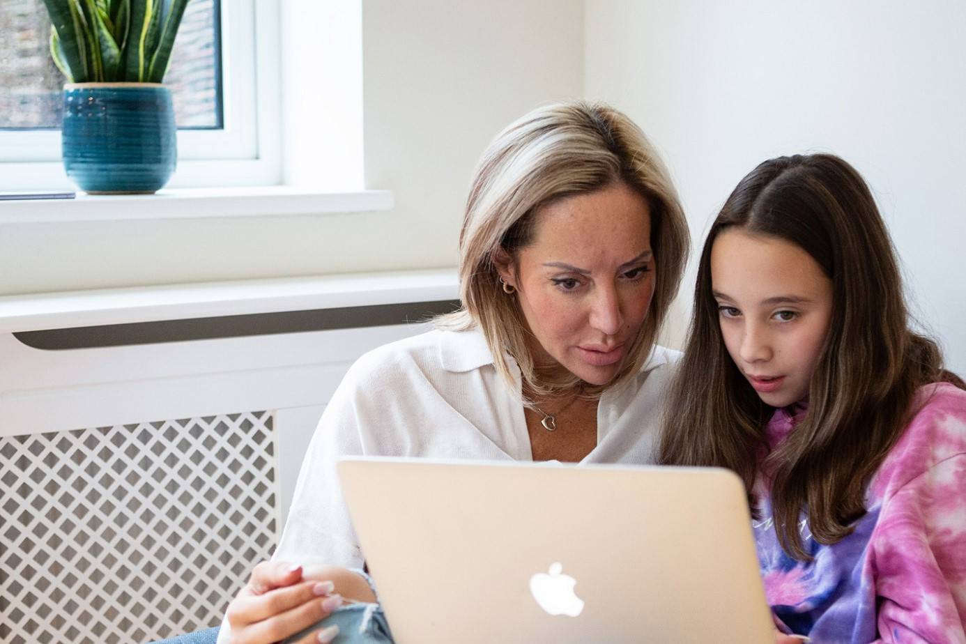 Young Girl And Woman Use Laptop Together While Cuddled On Chair