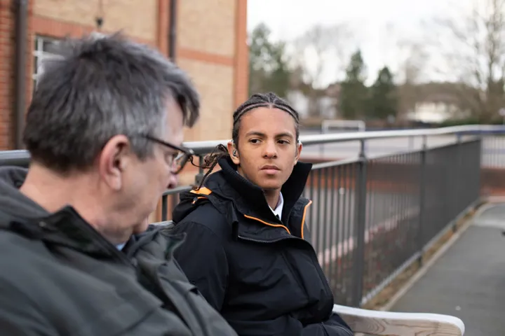 Student And Teacher Chatting Outside School On Bench
