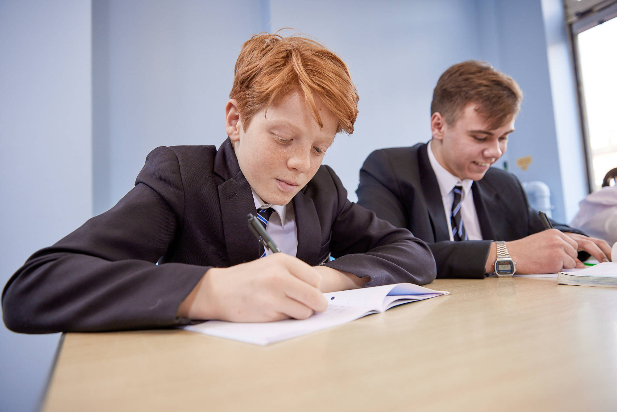 Two Young People Writing And Chatting At Desk