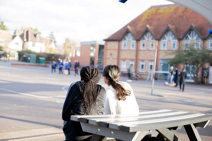 Young People On A Picnic Bench Looking At Playground