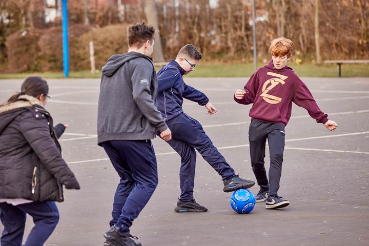 Young People Playing Football In Playground