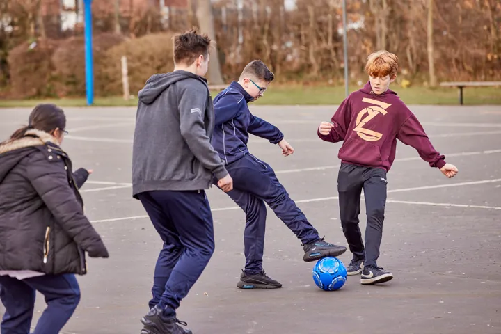 Young People Playing Football In Playground Young People Playing Football In Playground