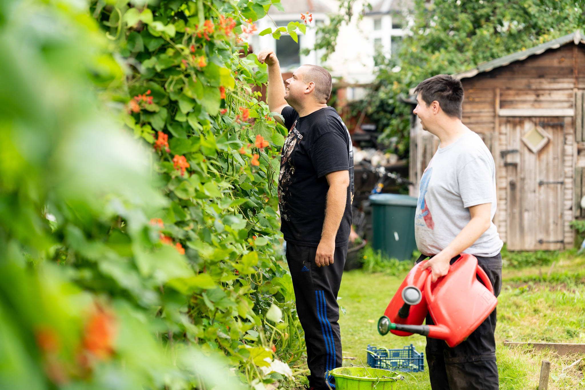 2 people inspecting their climbing beans at a Mind community garden. One is holding watering cans.