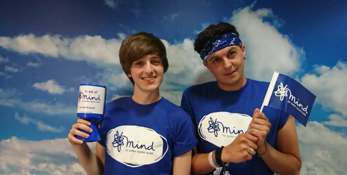 Two Mind fundraisers wearing Mind t-shirts and holding flags and money tins