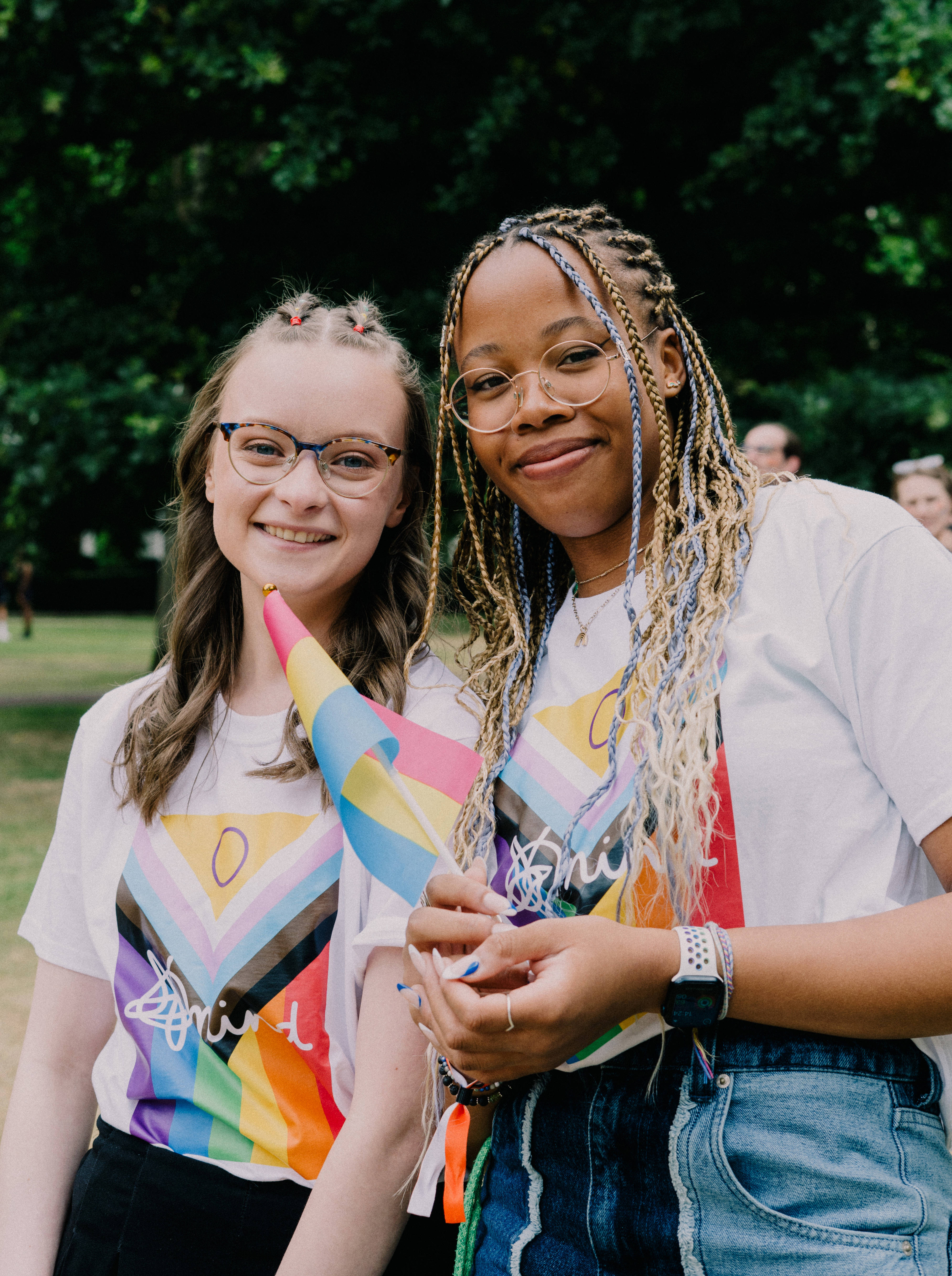 London pride Ellie and another Pride attendee smiling holding flags and wearing Mind Pride flag tshirts