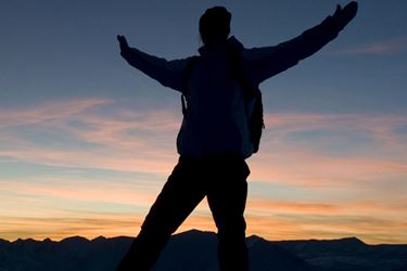 Trekker celebrating at peak of Snowdon against a sunrise