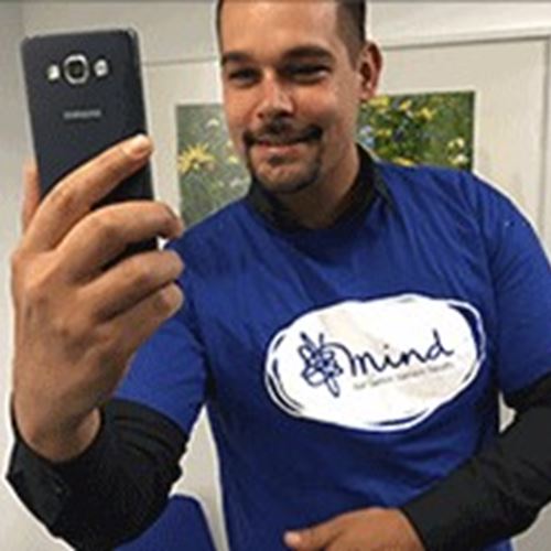Jay wears a Mind t-shirt and takes a selfie on his smart phone