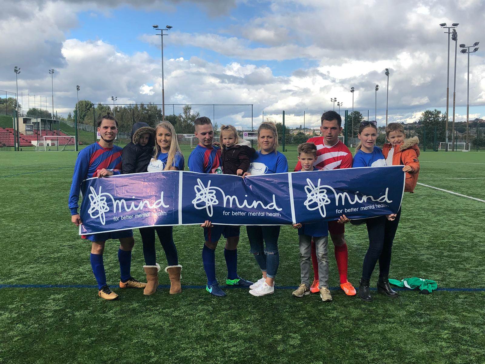 Mind fundraisers holding up Mind banner in football field