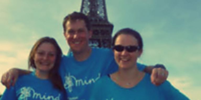 Mark in front of the Eiffel Tower wearing a Mind t-shirt with his arms around two others wearing the same top