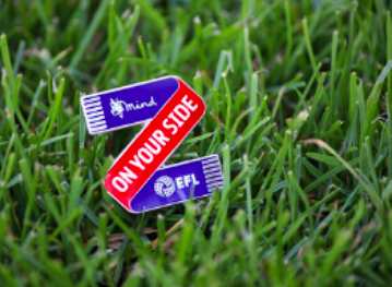 Blue and red pin badge on grass, saying on your side with mind and elf logos