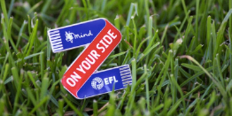 Blue and red pin badge on grass, saying on your side with mind and elf logos