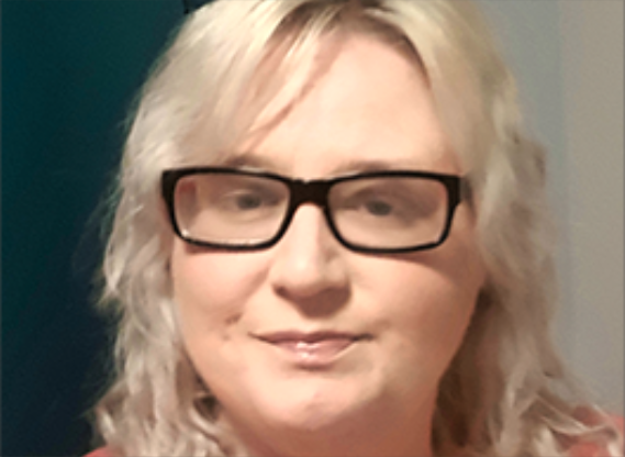 Girl with blonder hair and thick black framed glasses facing the camera