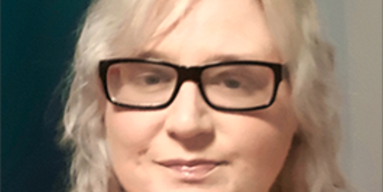 Girl with blonder hair and thick black framed glasses facing the camera