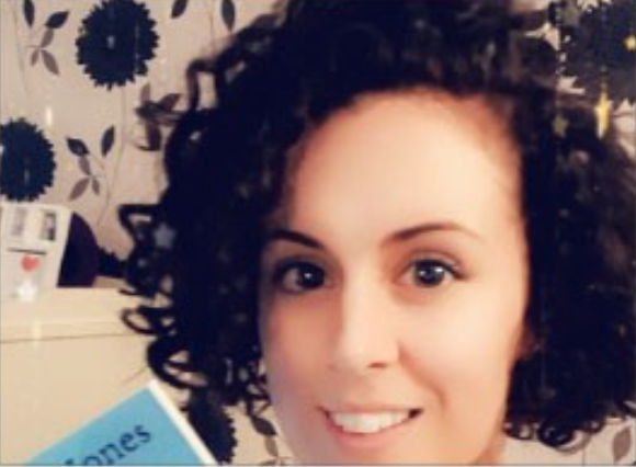 Woman was short curly dark brown hair smiling at the camera